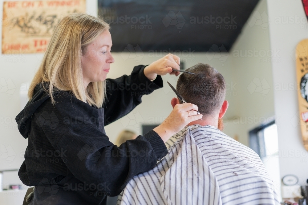 A woman barber cutting a man's hair behind his head - Australian Stock Image
