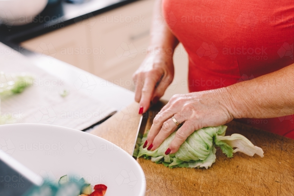 A woman chopping lettuce with a knife in a kitchen - Australian Stock Image