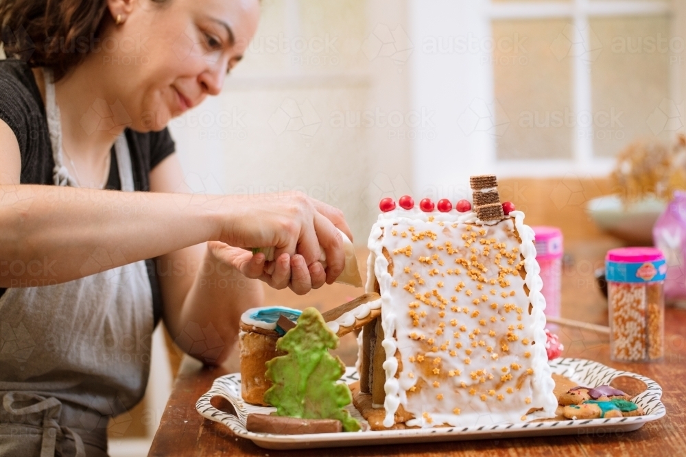 A woman decorating a homemade gingerbread house with figurines - Australian Stock Image