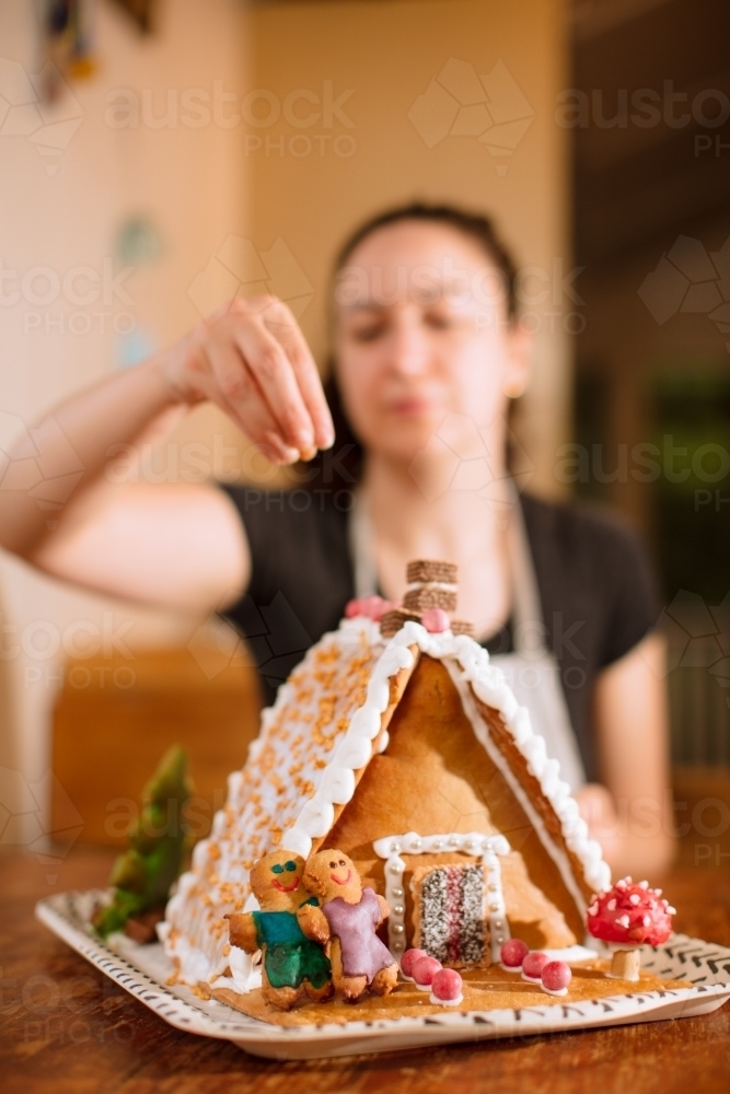 A woman decorating a homemade gingerbread house with figurines - Australian Stock Image