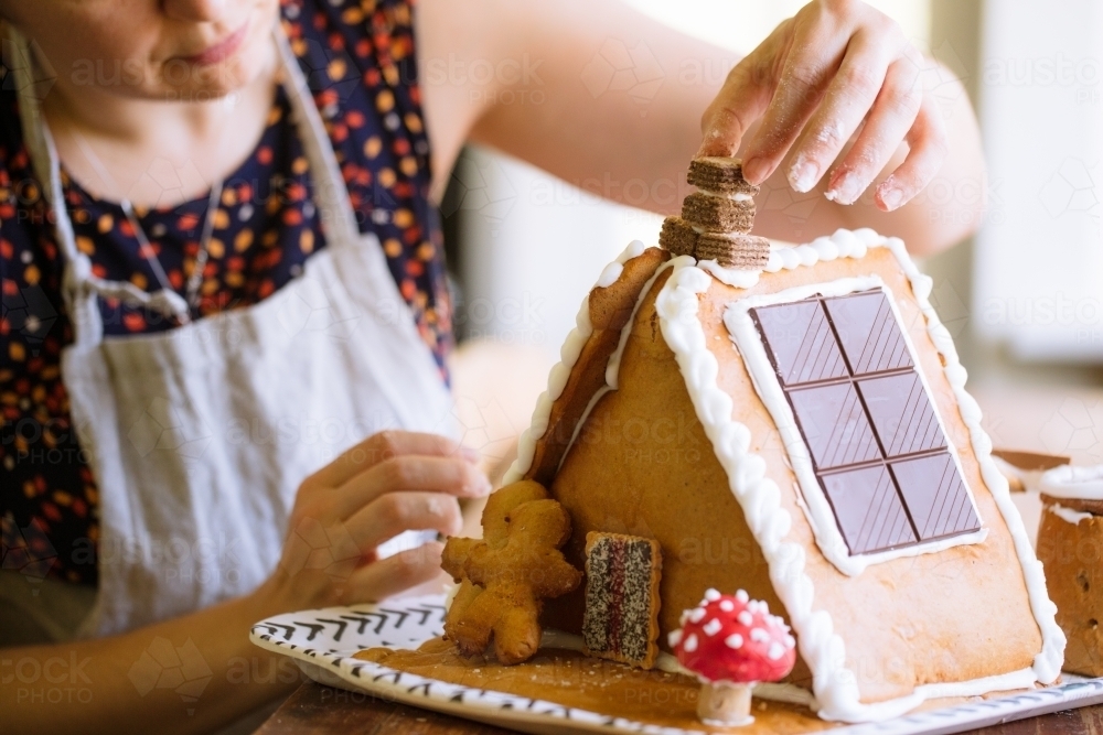 A woman decorating a homemade gingerbread house with figurines for Christmas - Australian Stock Image