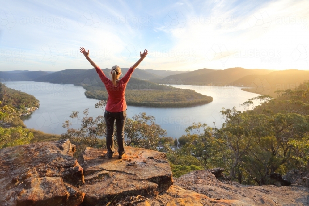A woman enjoys the warm golden sunlight in the afternoon and cliff top views across the mountains an - Australian Stock Image