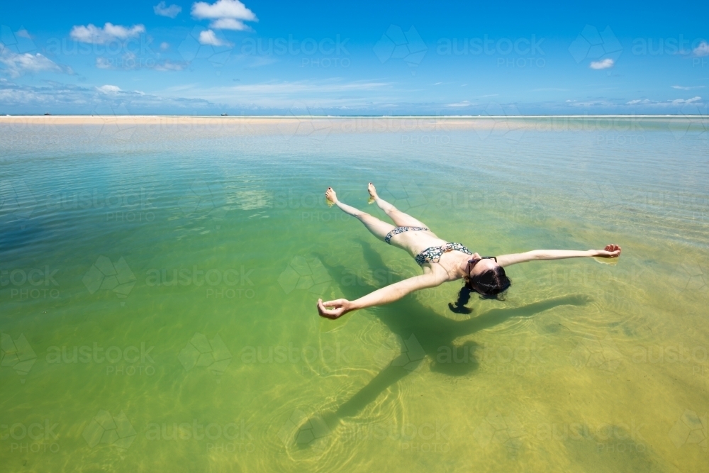 A woman floats in a pool of seawater by the sunny beach on Moreton Island - Australian Stock Image