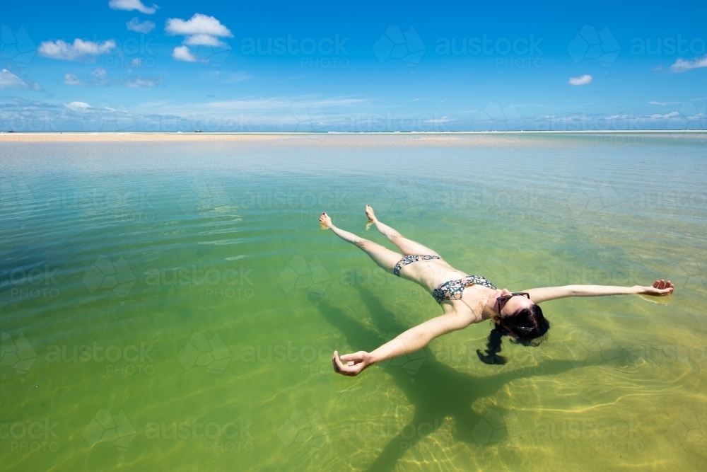 A woman floats in a pool of seawater by the sunny beach on Moreton Island - Australian Stock Image