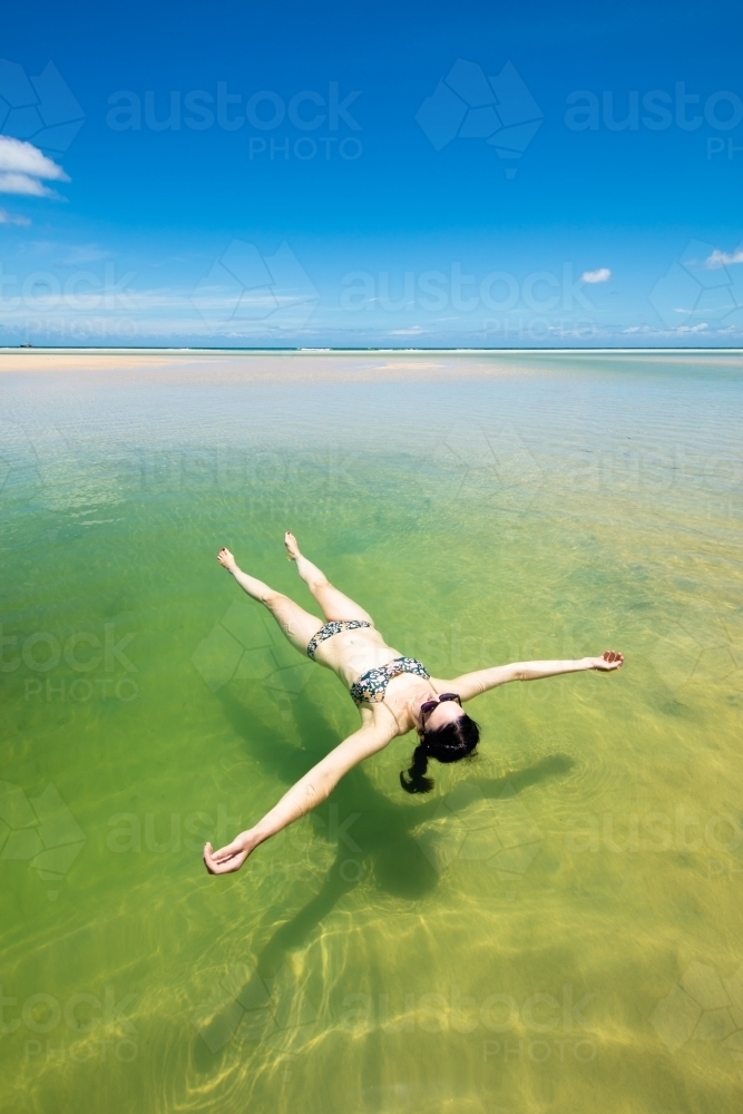 A woman floats in a pool of seawater by the sunny beach on Moreton Island - Australian Stock Image