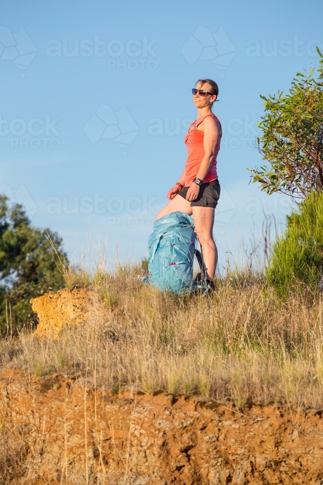 Image of A woman hiker standing with a backpack on a hilltop - Austockphoto