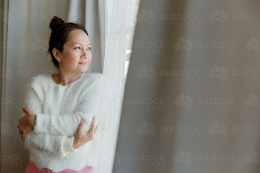 A woman in deep thought standing next to the window - Australian Stock Image