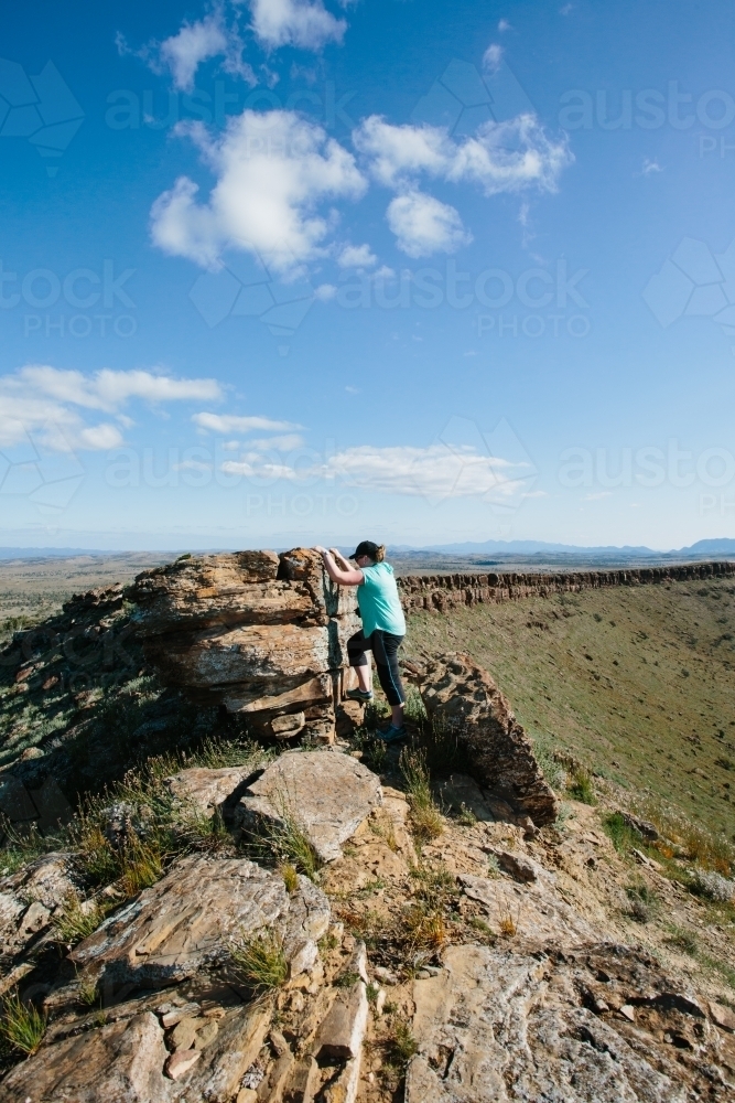 A woman in hiking gear clambering up rocks in the rugged landscape of the Flinders Ranges - Australian Stock Image