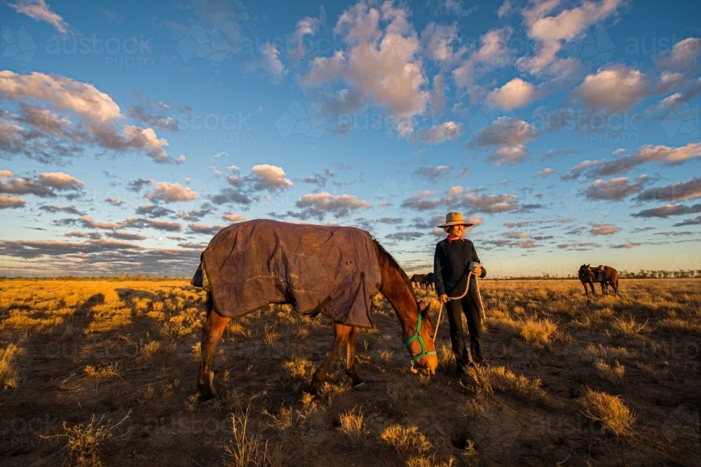 A woman lets a horse graze before a country race meeting - Australian Stock Image