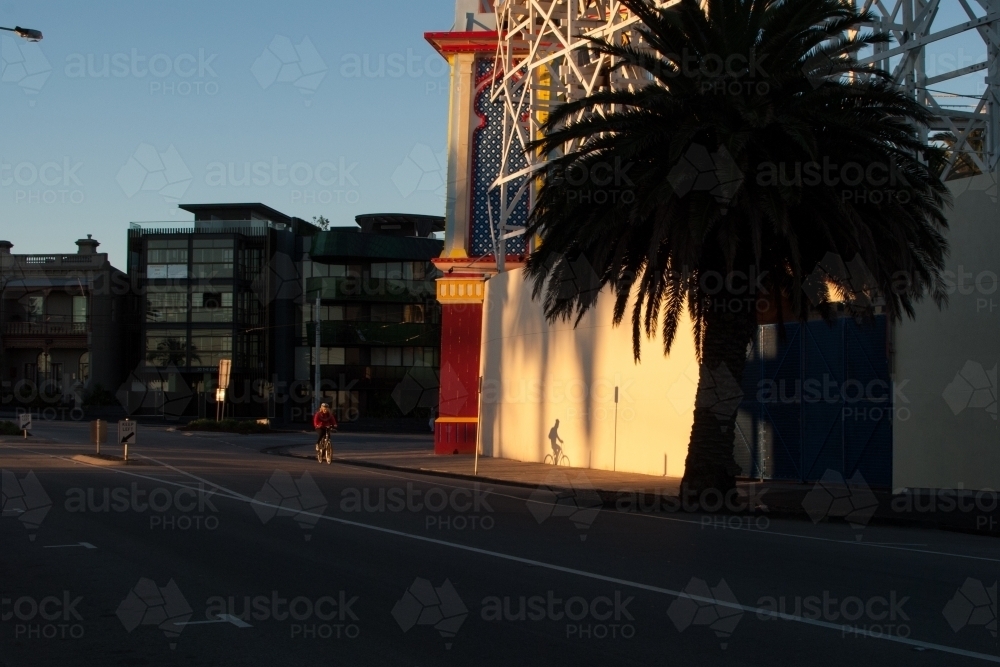 A woman's shadow is cast onto Luna Park in St Kilda as she rides by - Australian Stock Image