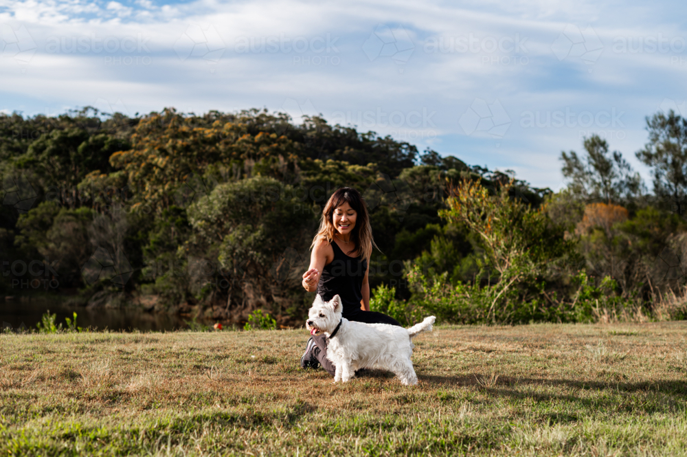 Image of A woman smiles and plays with her dog in a park surrounded by ...