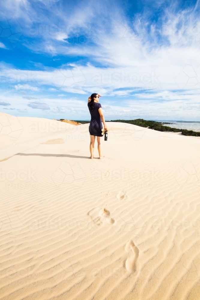 A woman stands high on a sand dune viewing into the distance of Moreton Bay. - Australian Stock Image