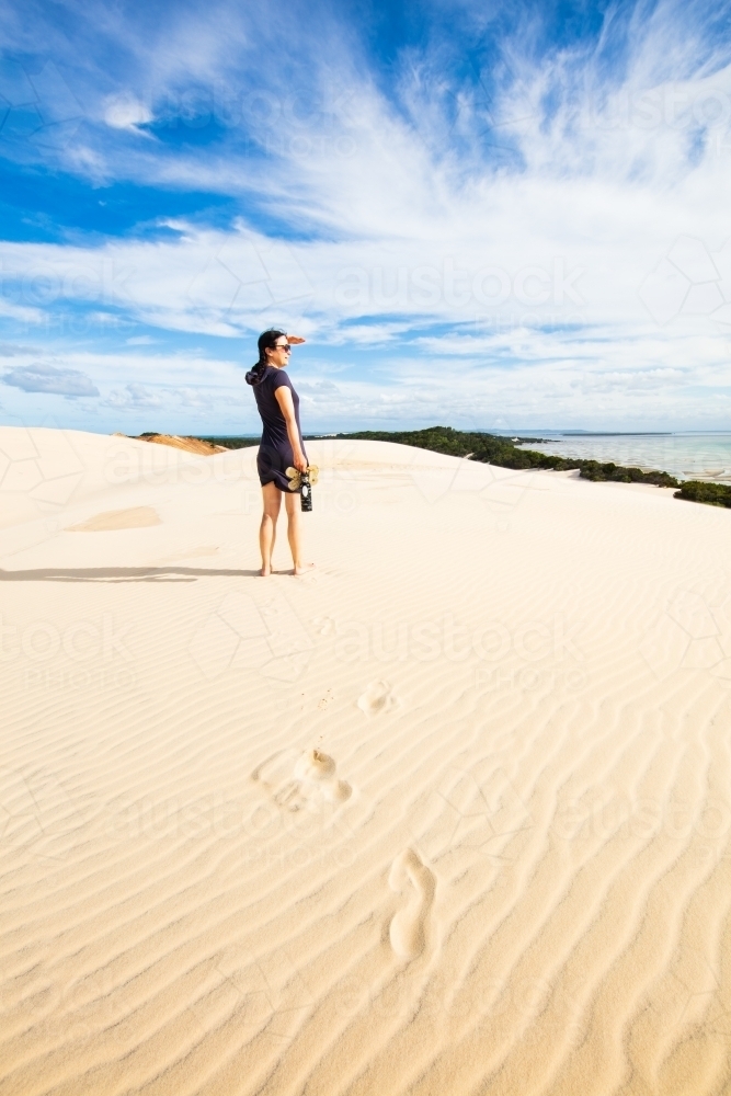 A woman stands high on a sand dune viewing into the distance of Moreton Bay. - Australian Stock Image