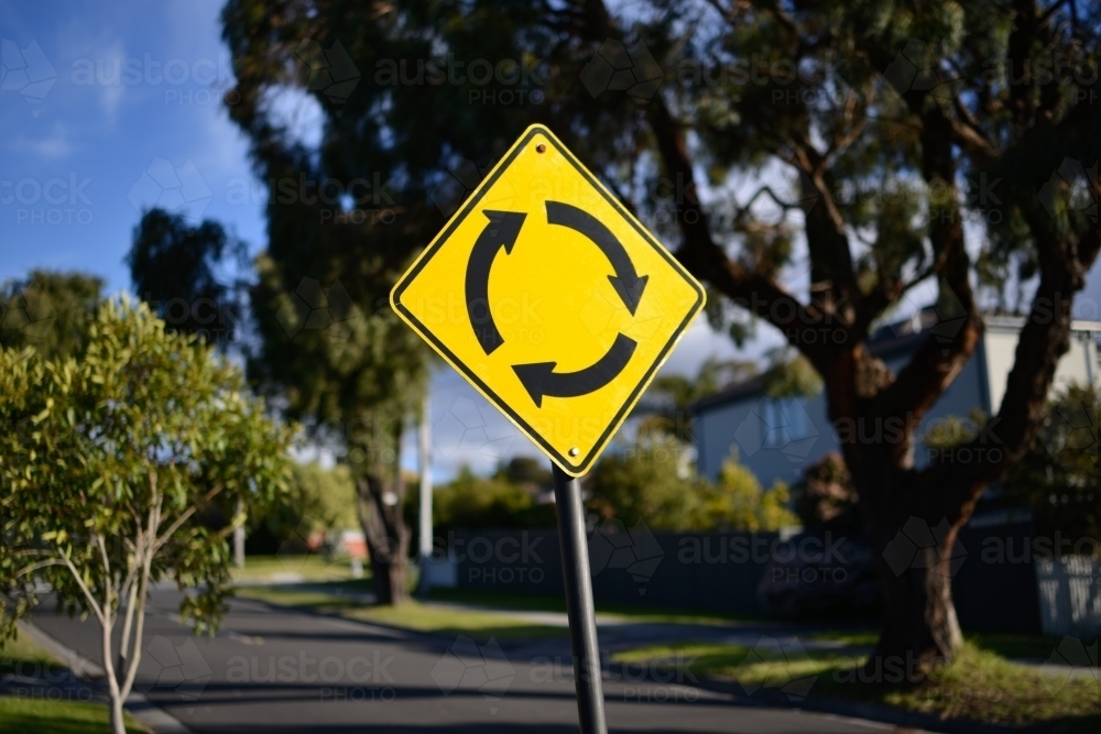 A yellow roundabout street sign bathed in sunlight - Australian Stock Image