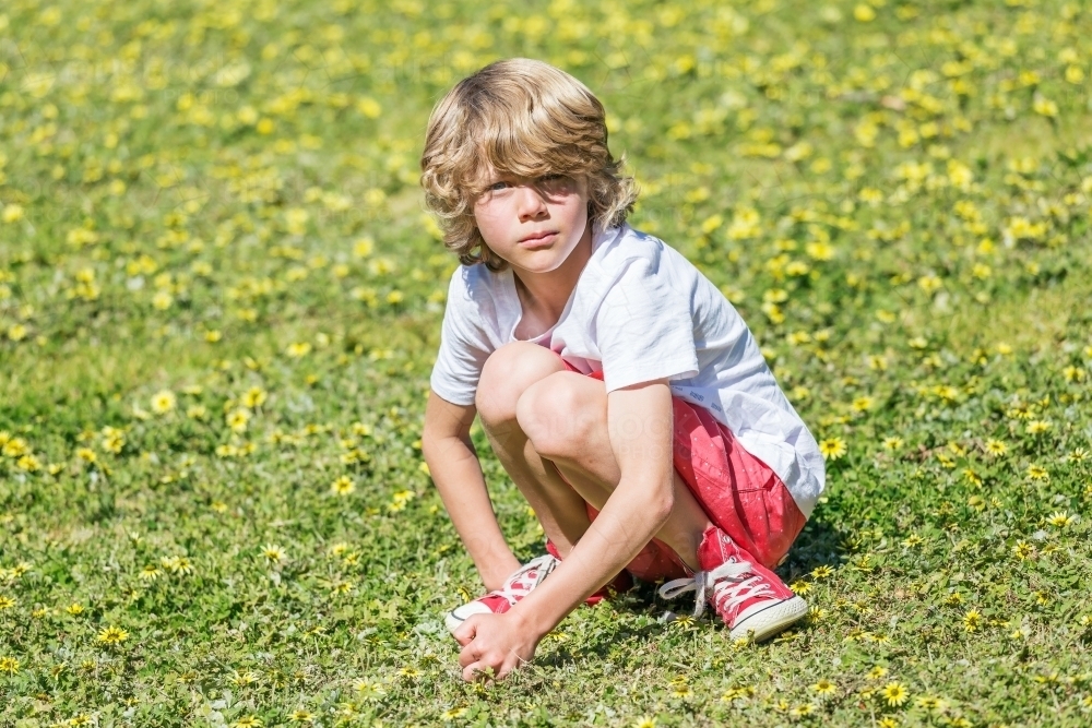 A young boy crouching on grass in a park - Australian Stock Image