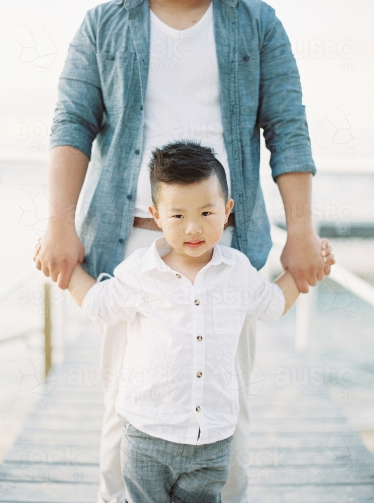 A young boy holding hands with his father walking a long a wharf - Australian Stock Image