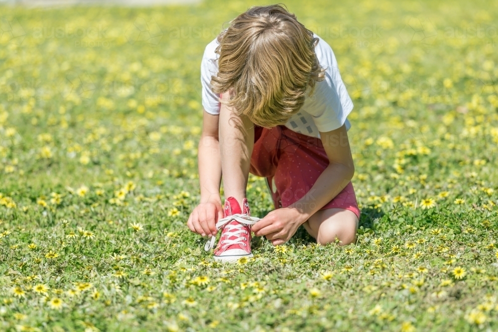 A young boy kneeling down on grass tying his shoe laces - Australian Stock Image
