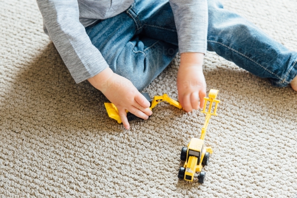 A young boy playing with a small yellow toy digger - Australian Stock Image