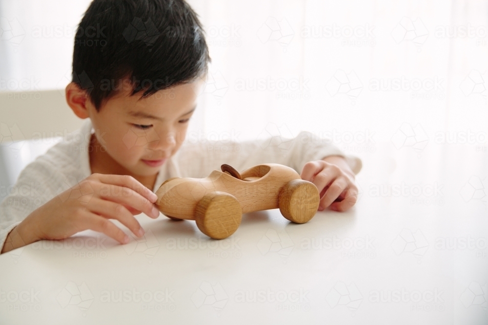 A young boy playing with his wooden car at home sitting at the table - Australian Stock Image