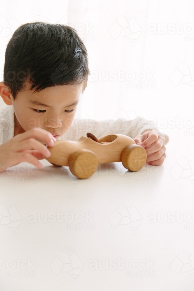 A young boy playing with his wooden car at home sitting at the table - Australian Stock Image