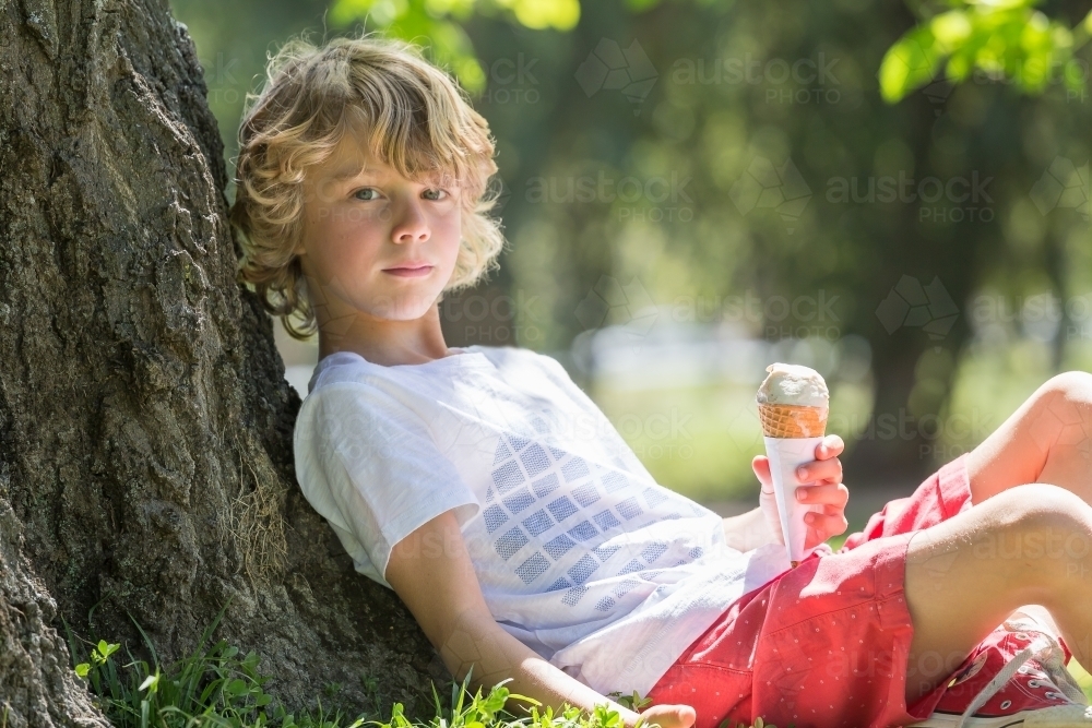A young boy relaxing against a tree with an ice cream - Australian Stock Image