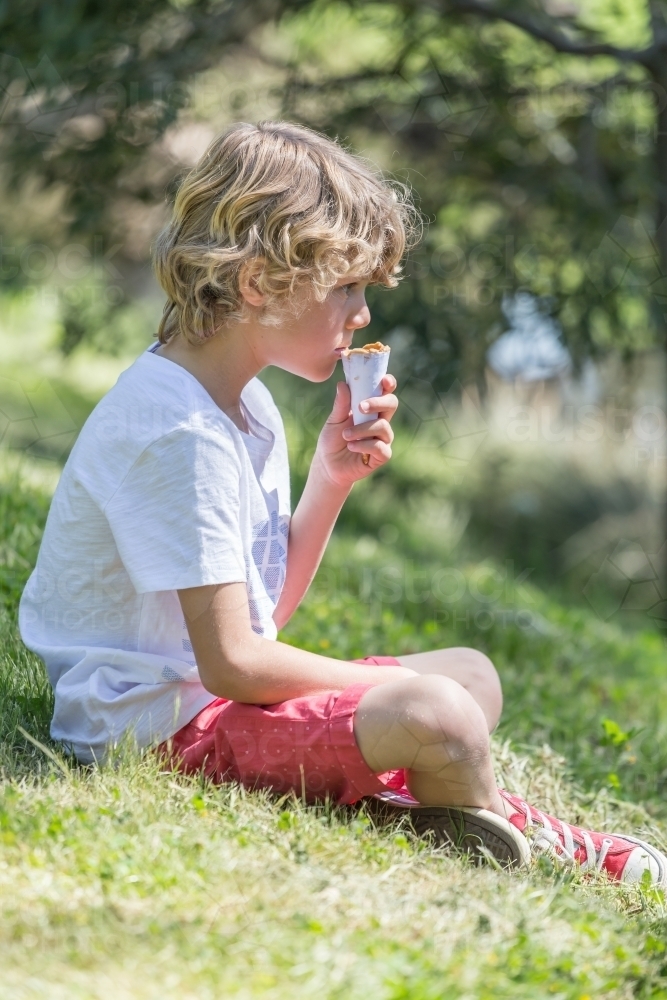 A young boy sitting in a park eating an ice cream cone - Australian Stock Image