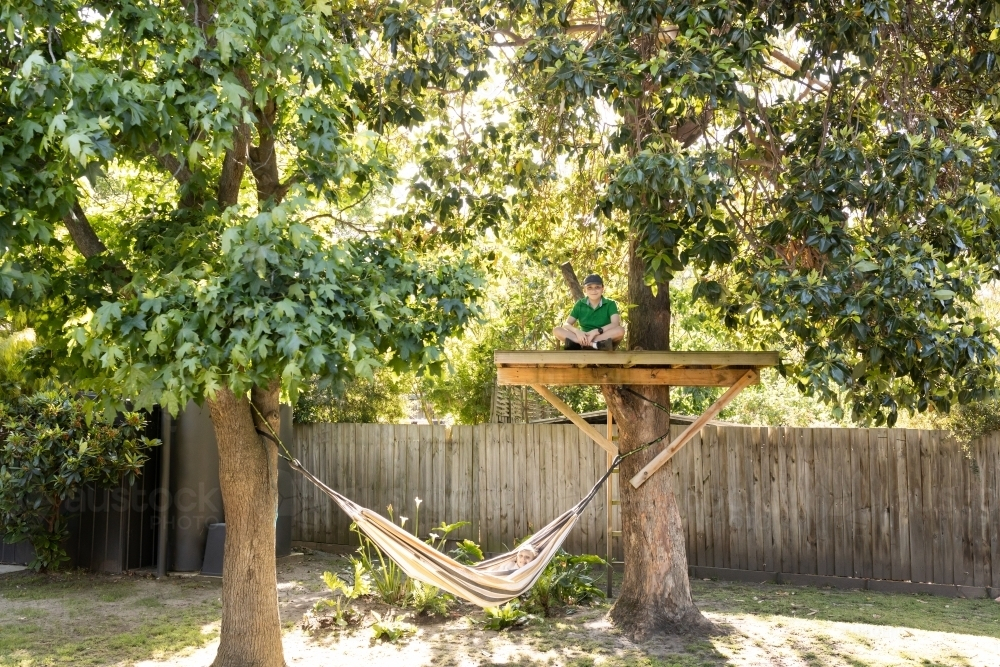A young boy sitting in a tree house and a girl lying in a hammock in an australian backyard - Australian Stock Image