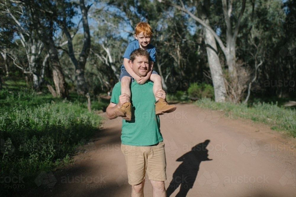 A young boy sitting on his fathers shoulders in the bush - Australian Stock Image