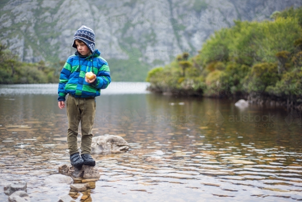 A young boy standing on a rock in a river - Australian Stock Image