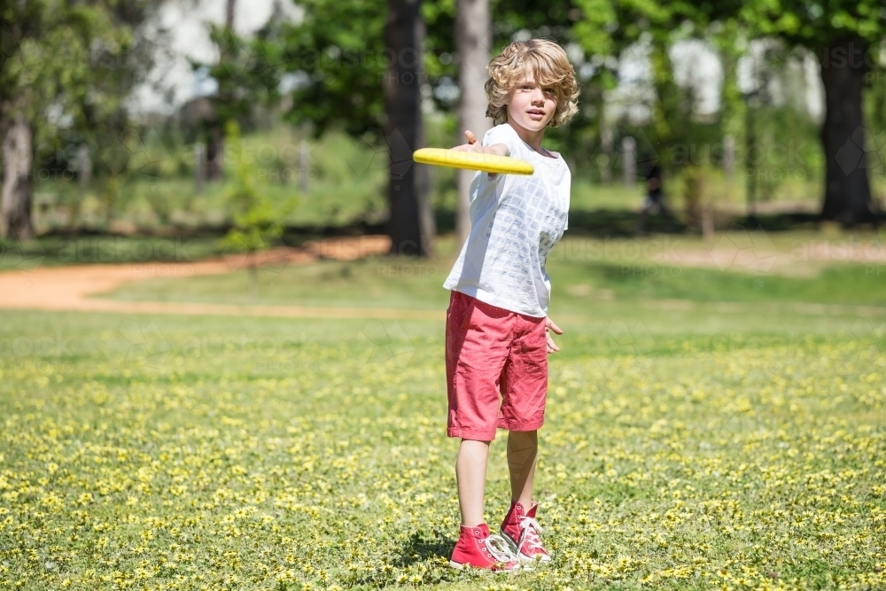 A young boy throwing a frisbee in the park - Australian Stock Image