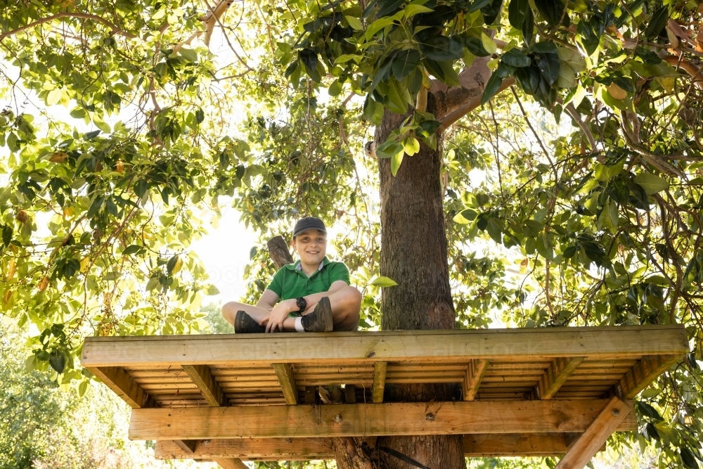 A young boy wearing a hat sitting in a backward tree house in an australian backyard - Australian Stock Image