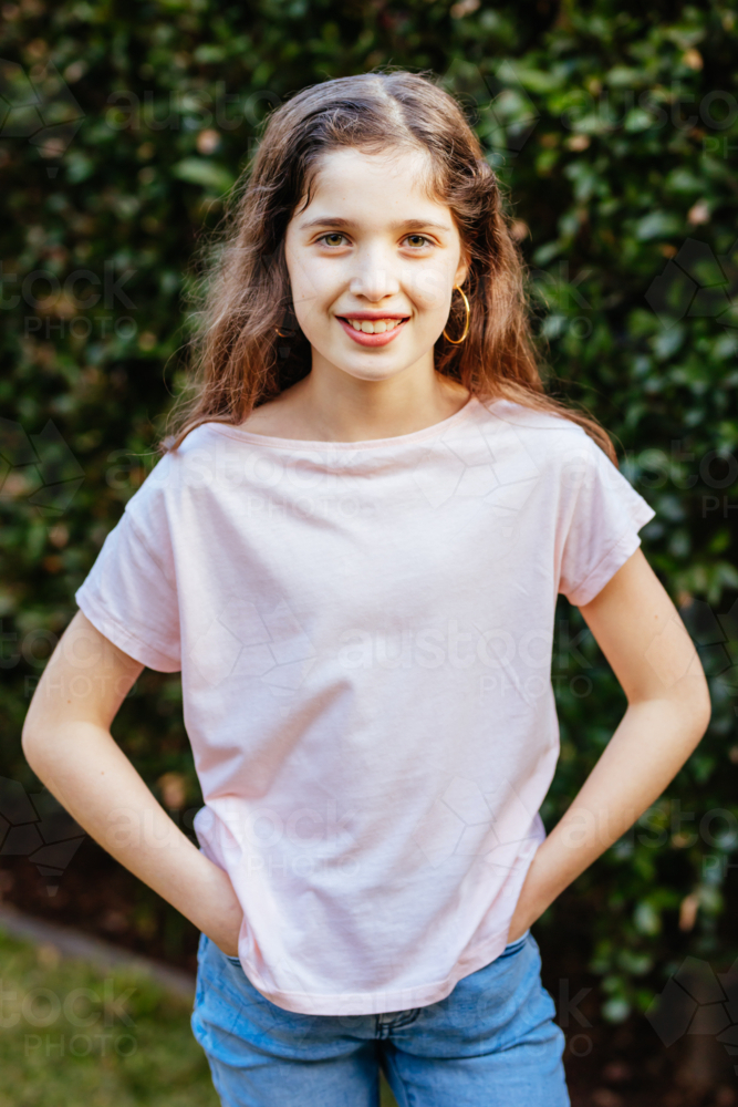 A young caucasian girl poses in front of a green hedge on a sunny evening in Australia - Australian Stock Image