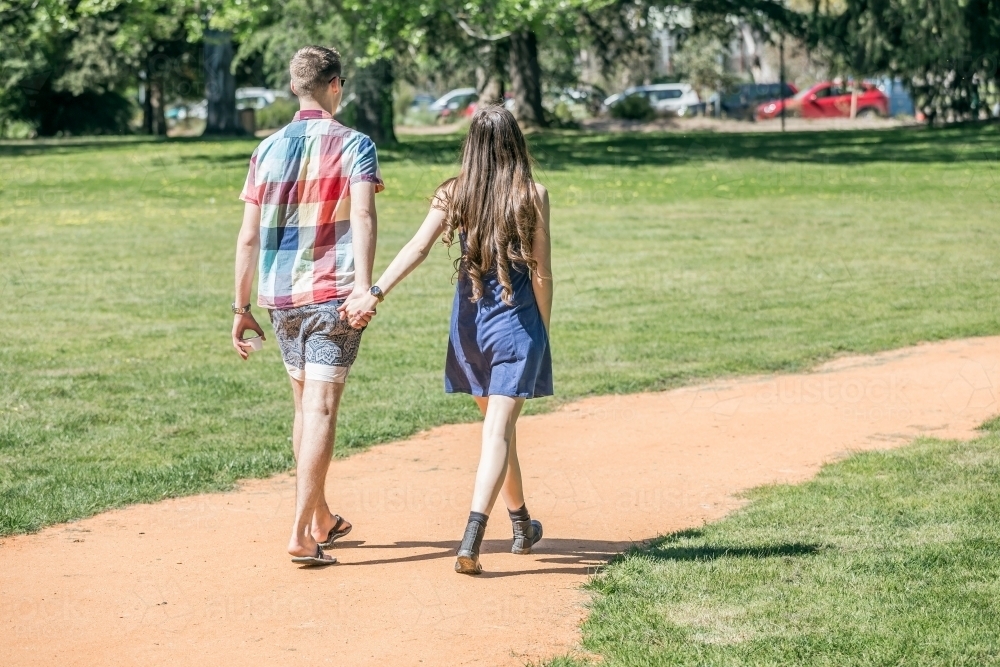 A young couple walk hand in hand around a park track - Australian Stock Image