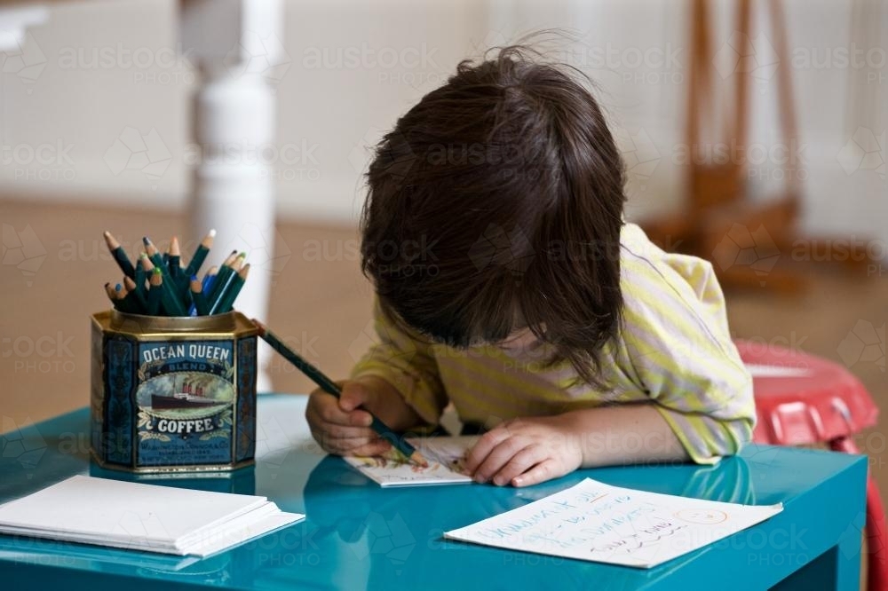 A young girl / child sits at a desk drawing with pencils - Australian Stock Image