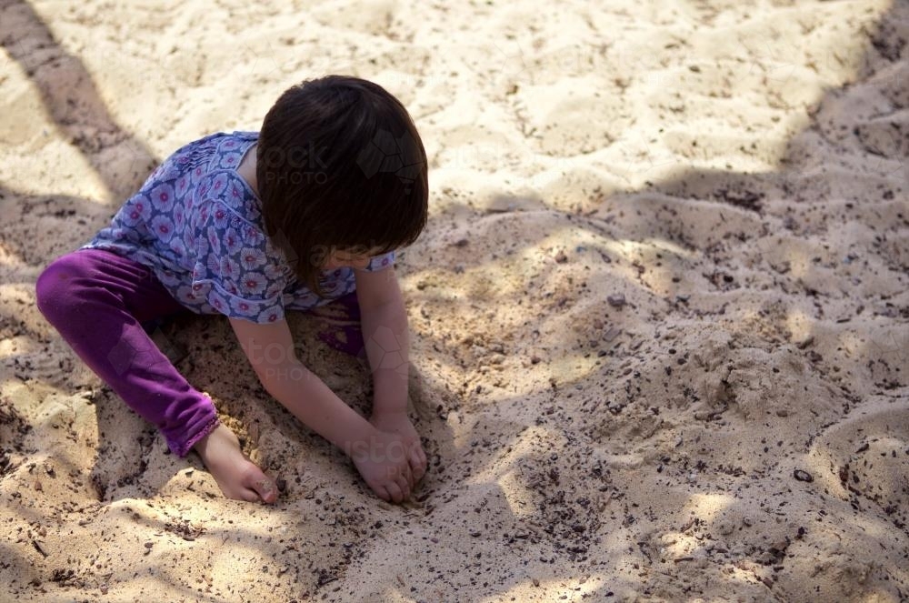 A young girl playing in the sand, digging for treasure in a sandpit - Australian Stock Image