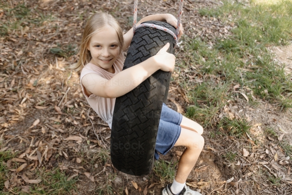 A young girl sitting on a home made tyre swing playground - Australian Stock Image