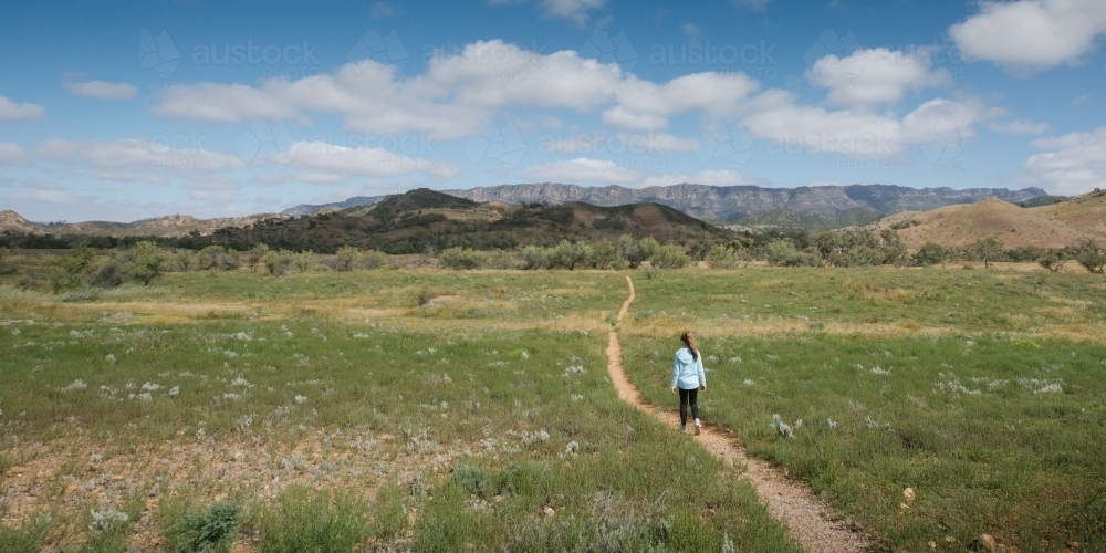 A young girl walking down a single bush trail towards a mountain range - Australian Stock Image