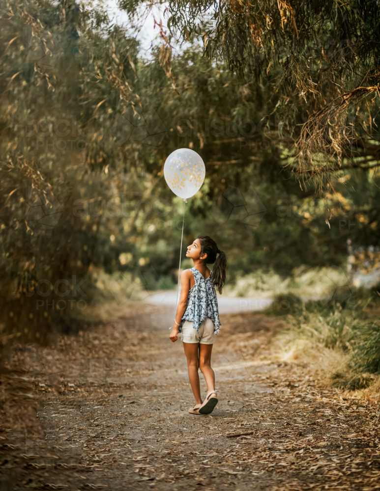 A young girl walking holding a white balloon - Australian Stock Image