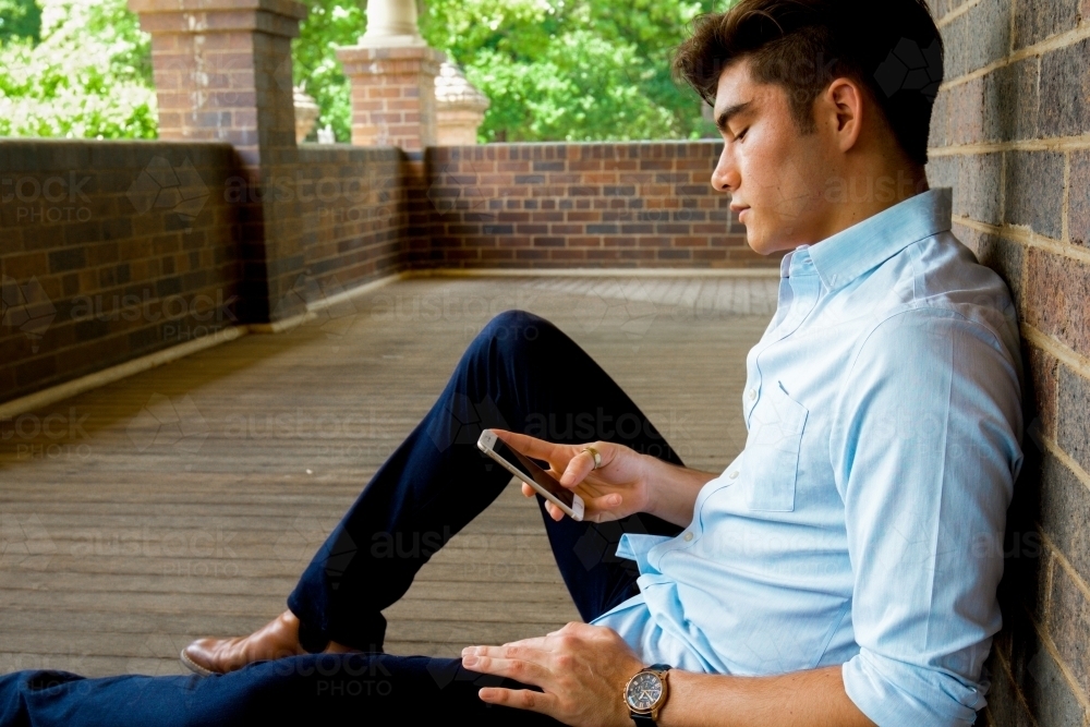 A young male sitting on the ground on a covered verandah - Australian Stock Image