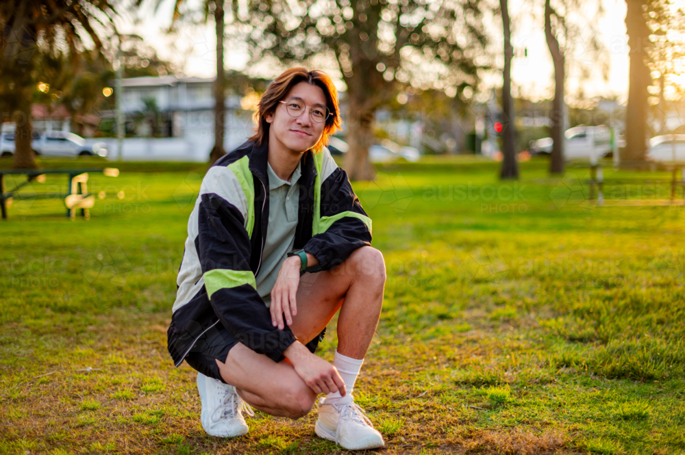 A young man poses in a park at sunset, sporting casual athletic wear and enjoying the moment - Australian Stock Image