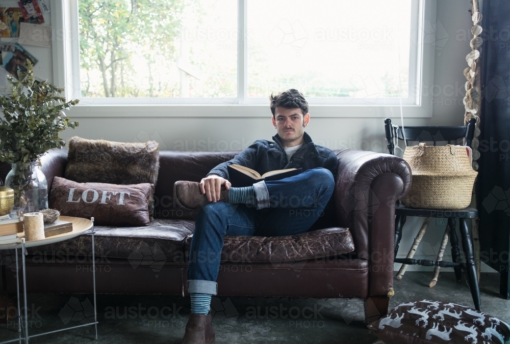 A young man reading a book looks up at the camera. - Australian Stock Image