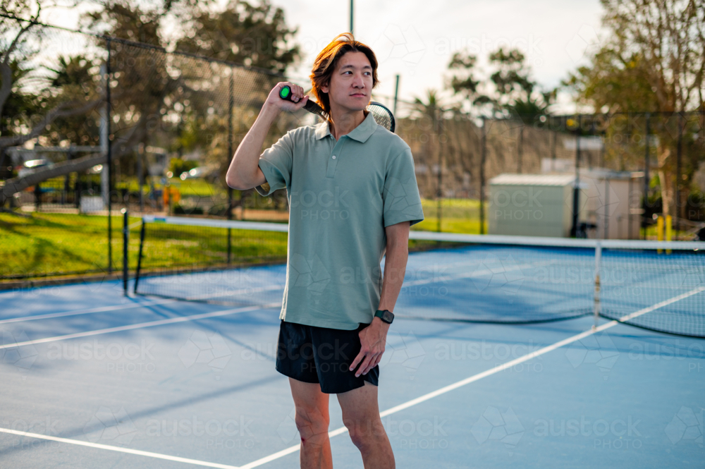 A young man stands confidently on a blue tennis court - Australian Stock Image