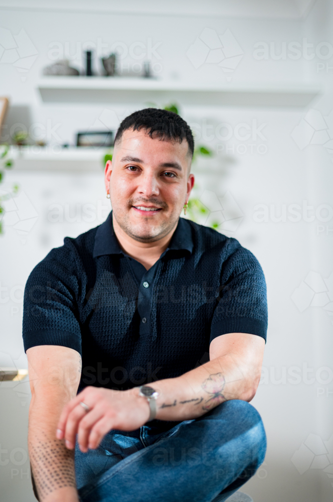 A young man with short hair sits comfortably, looking cheerful in stylish clothes. - Australian Stock Image