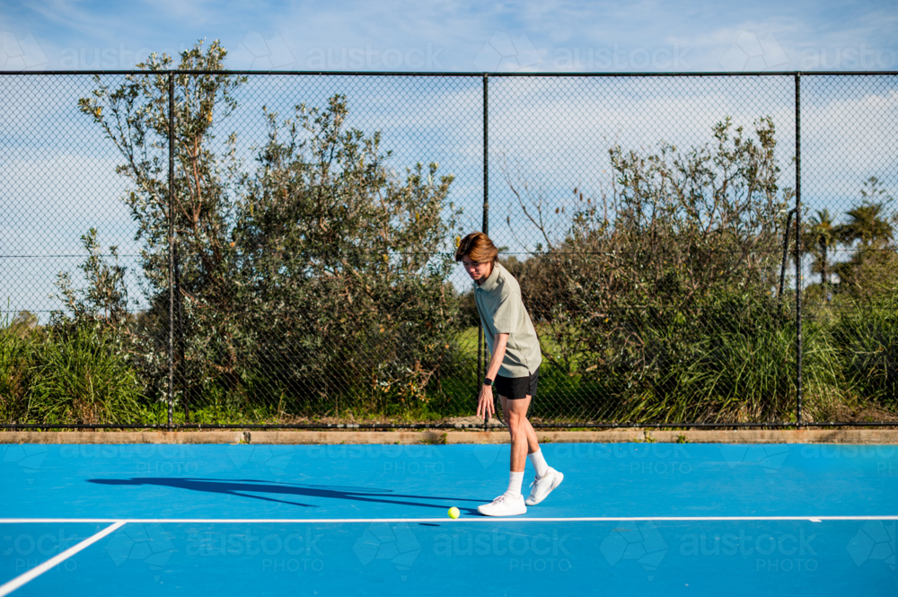 A young player in casual attire prepares to hit a tennis ball on a sunny day outdoors - Australian Stock Image