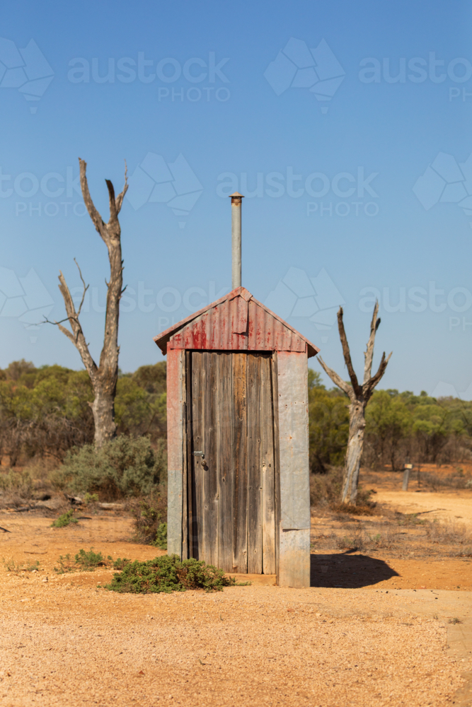 Abandoned outback outhouse in red dirt with blue sky - Australian Stock Image
