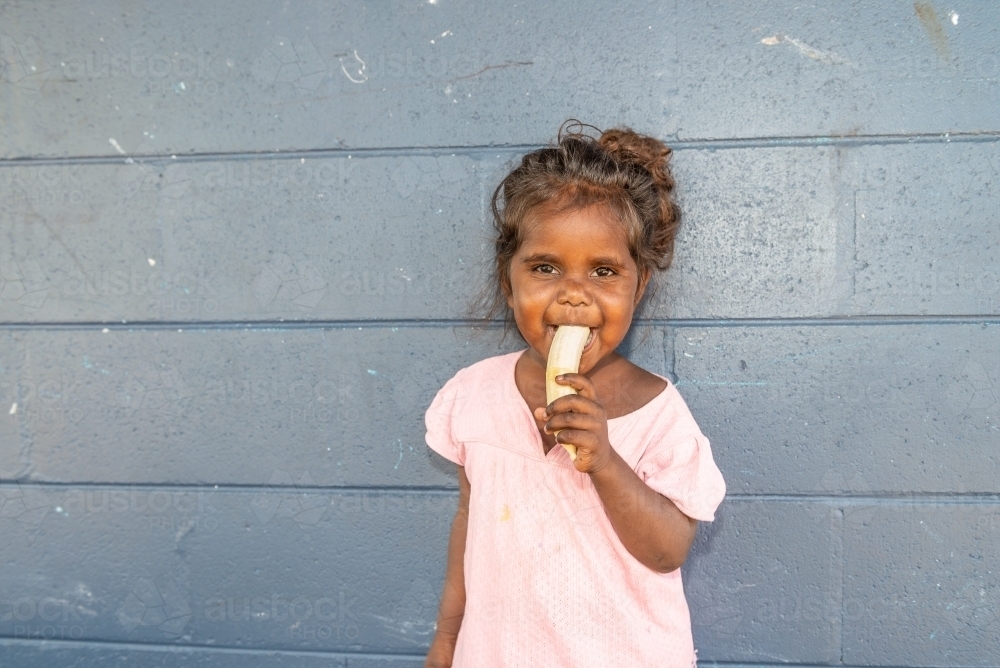 Aboriginal 3 year old girl eating a banana - Australian Stock Image