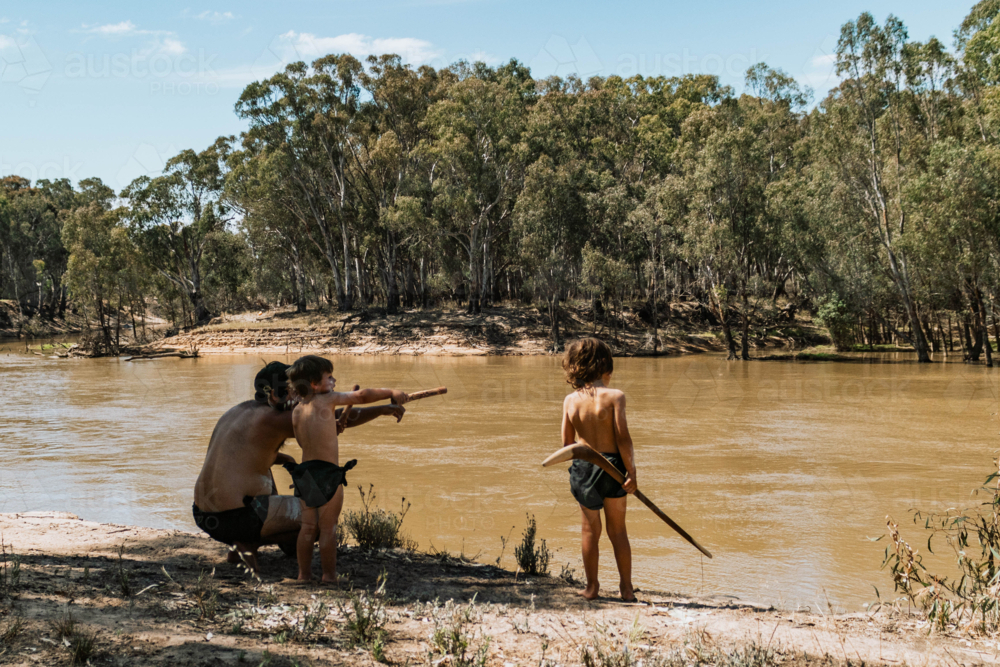 Aboriginal Australian father teaching children on banks of river - Australian Stock Image