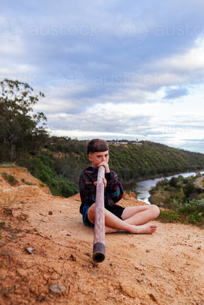 aboriginal boy playing didgeridoo in Australian landscape with view to Hunter River - Australian Stock Image