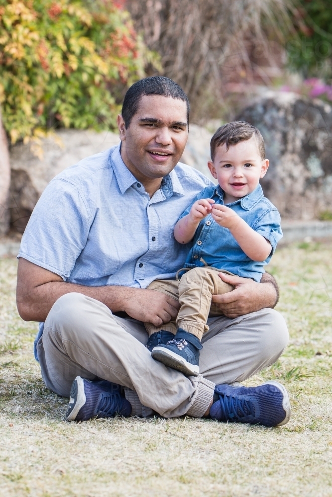 Aboriginal caucasian mixed race son sitting with father smiling - Australian Stock Image