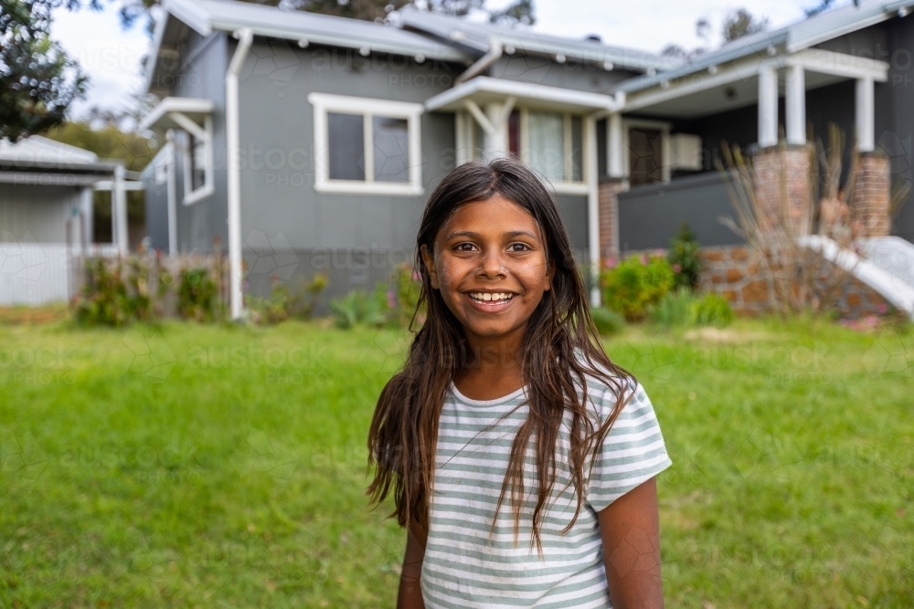 Aboriginal child in front of grey fibro house - Australian Stock Image